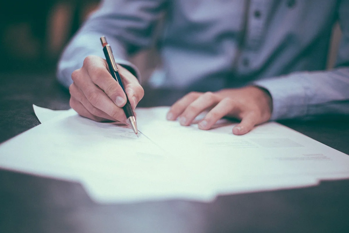 Person writing on legal documents at a dark desk with a black-and-gold pen