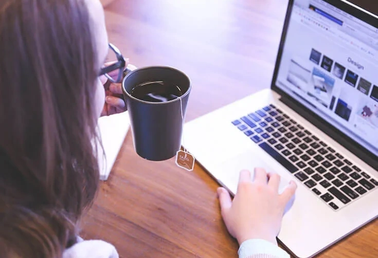 Person working on a laptop at a wooden table with a mug, researching asset protection