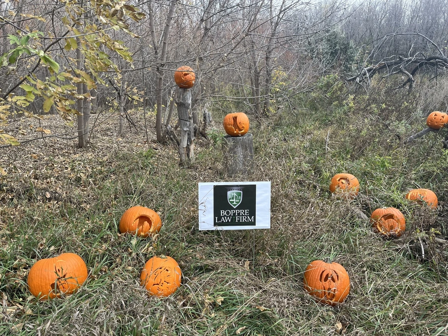 Carved pumpkins arranged around a white BOPPRE LAW FIRM sign on a woodland tree stump in autumn