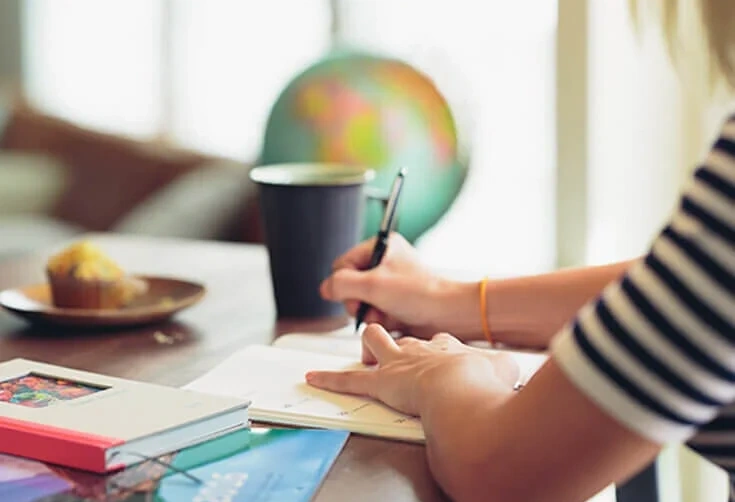 Person taking notes at a wooden table with a globe, books, and a coffee cup for estate planning
