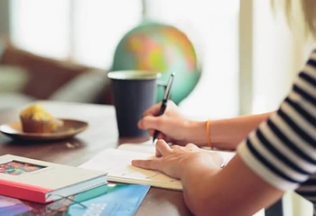 Person taking notes at a wooden table with a globe, books, and a coffee cup for estate planning