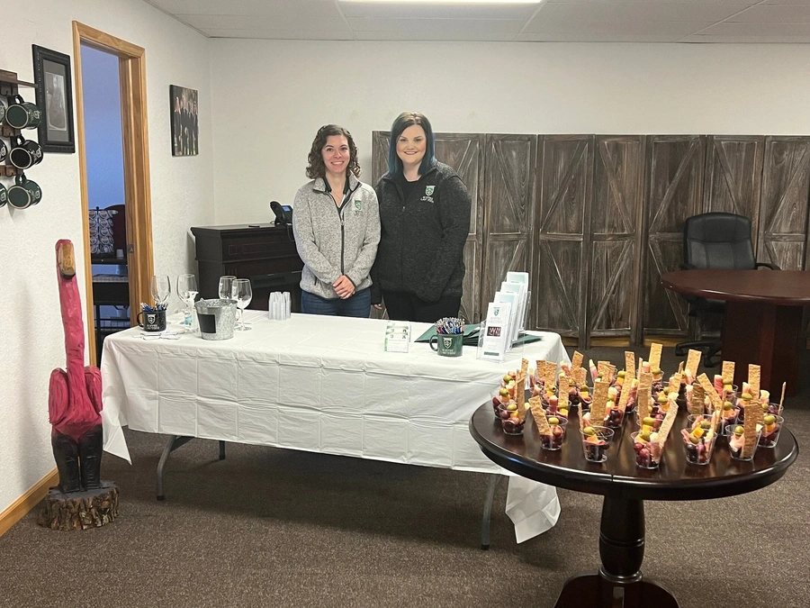 Volunteers at an indoor wine walk table with tasting glasses, fruit cups, and informational pamphlets