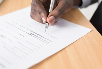 Hand signing a legal document with a silver fountain pen on a wooden desk