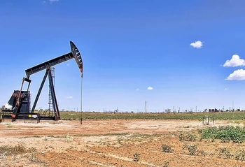 Black oil pumpjack standing in a dusty field under a clear blue sky, representing oil and gas operations