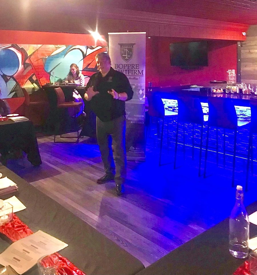 Presenter speaking at a Wills & Wine community event in a bar with graffiti wall and banner