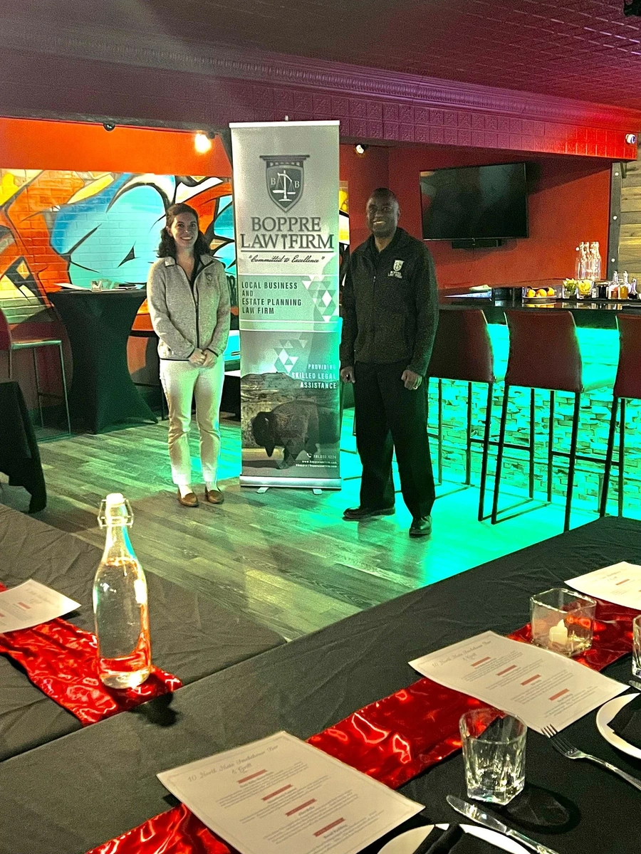 Two people beside a BOPPRE LAW FIRM banner at an indoor event with neon-lit bar and graffiti wall