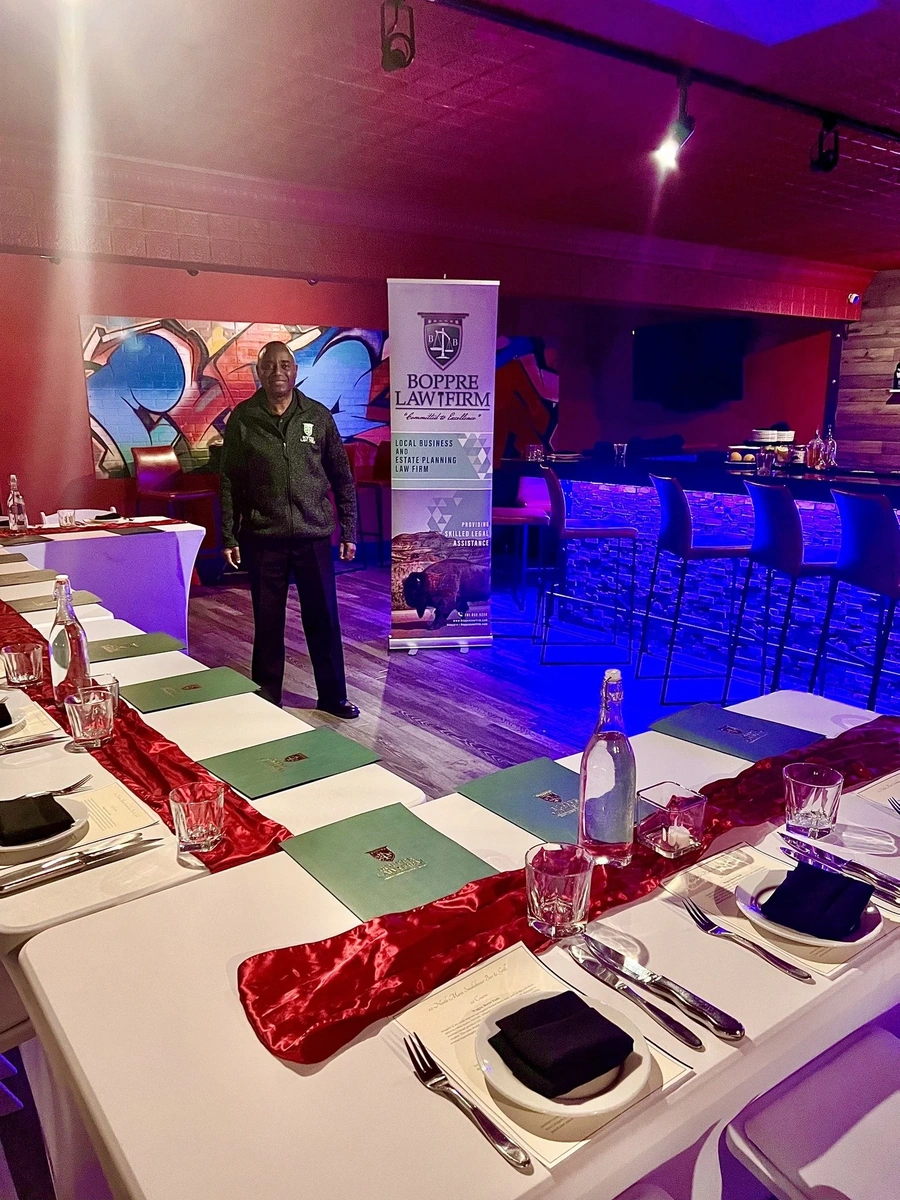 Man beside Boppre Law Firm banner at a formal dinner with banquet tables, glassware, and muraled bar behind.