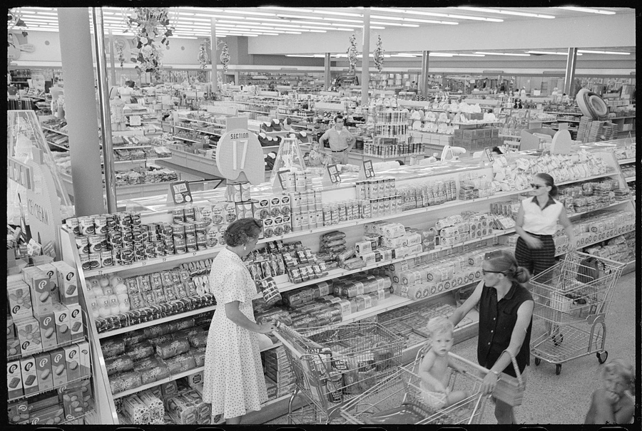 Customers moving through a large 1958 grocery store with shopping carts.