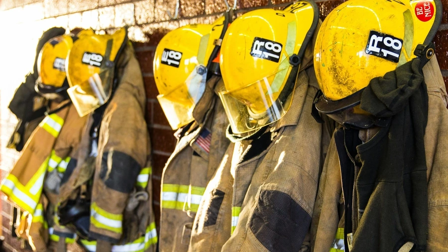 A row of firefighter turnout gear, including yellow helmets and coats, hanging on a rack.