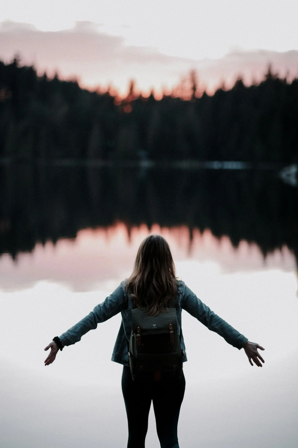 Woman with her arms out looking over a lake and dawn