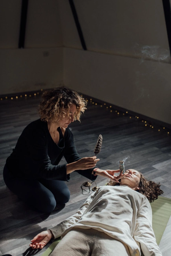 A practitioner performs a cleansing ritual using sage and feathers to promote healing and relaxation indoors.