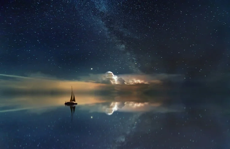 Sailboat in calm ocean at night with clouds and stars