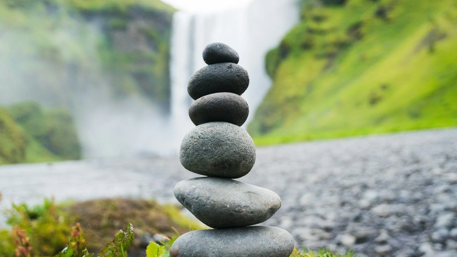 Rocks stacked vertically in front of a large waterfall int he background