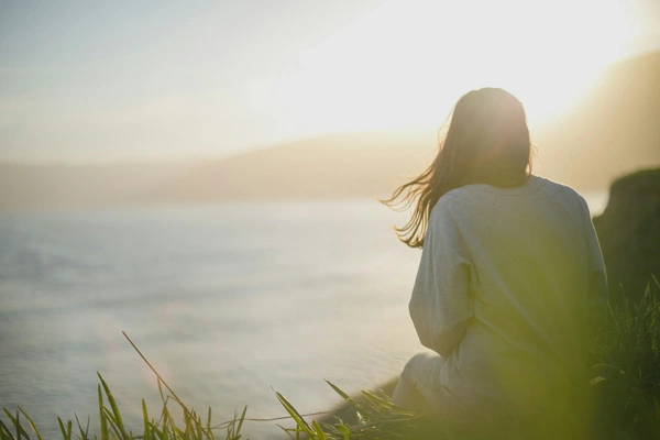 Woman looking over ocean with her hair blowing in the wind