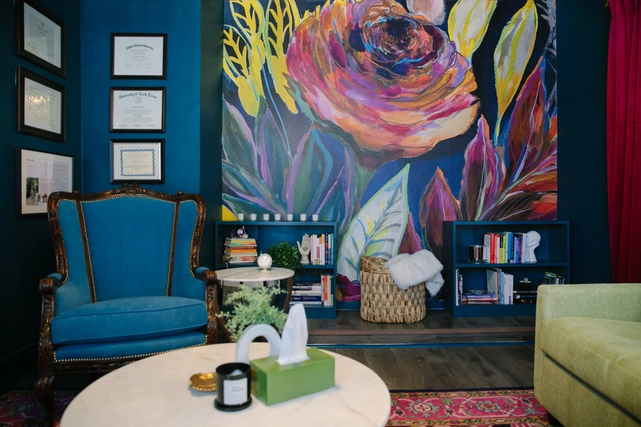 Cozy therapy room with a colorful mural, bookshelves, a table with tissues, a stylish chair and couch