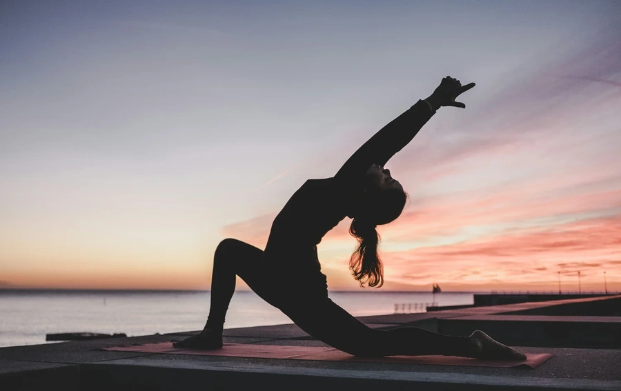 Woman doing a yoga pose by a lake at sunset
