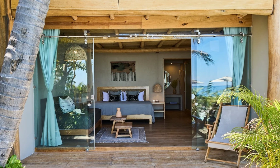 Wellness retreat bedroom with glass sliders open to the side reflecting palm trees and the ocean