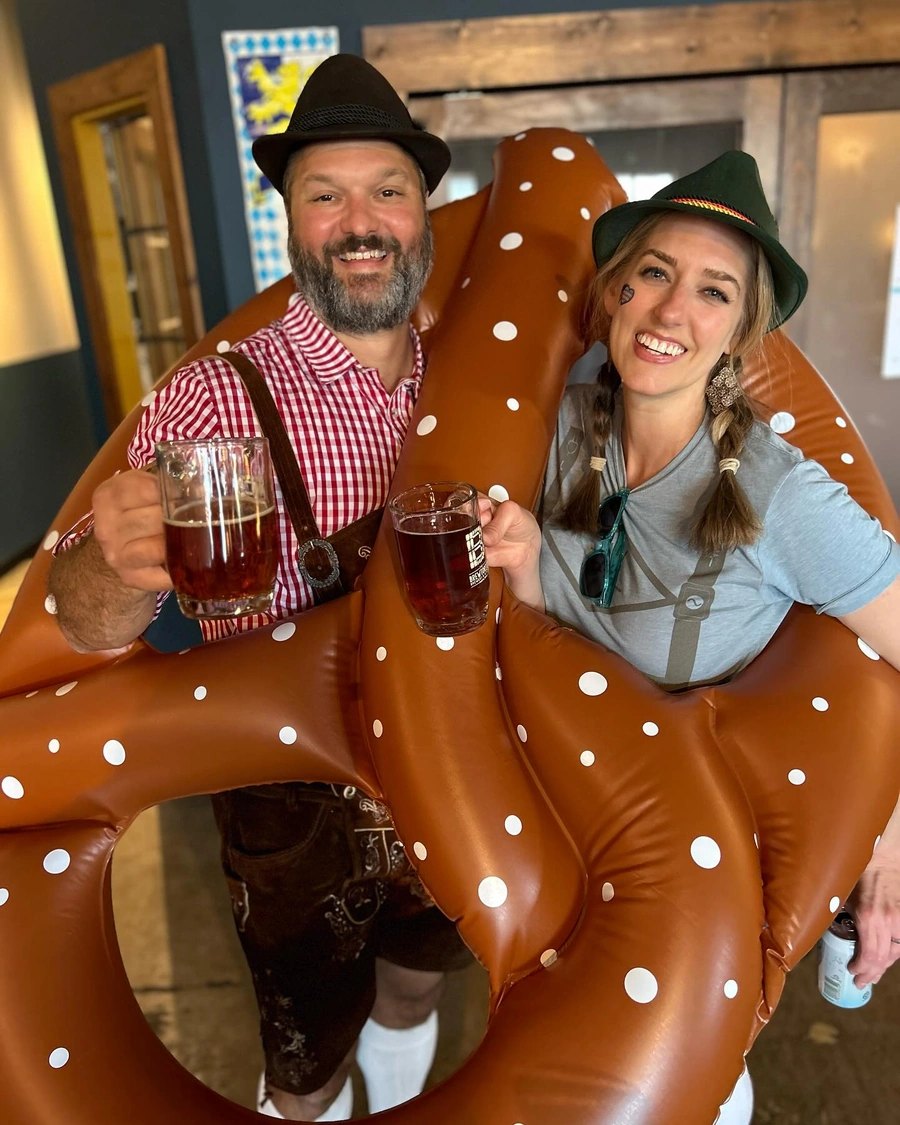 Brewtorium owners celebrating Oktoberfest in traditional German attire, surrounded by authentic decorations and festive atmosphere