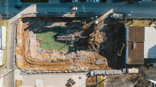 Aerial view of commercial grading and excavation work with excavators and dump trucks at an urban construction site.