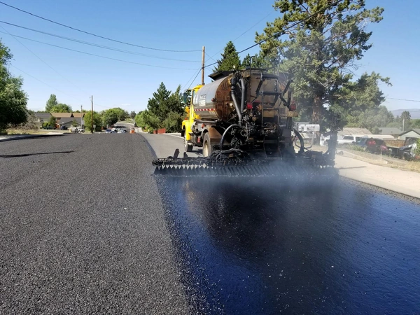 Road construction in Redmond, OR, with asphalt paving equipment. Sunny weather highlights the process.