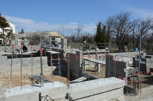 Workers building concrete block retaining walls with rebar and scaffolding at a commercial construction site.