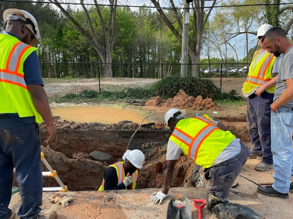 Team of construction workers inspecting an underground utility site on a sunny day.