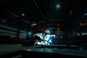 A welder working on steel structures in a large industrial warehouse, emitting bright sparks.