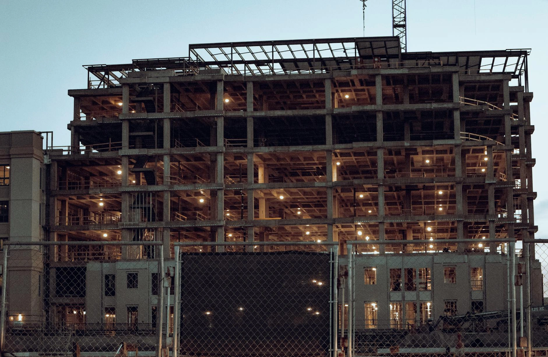Multi-story commercial building under construction at dusk in Fort Worth, Texas, illuminated by work lights with a crane on top.