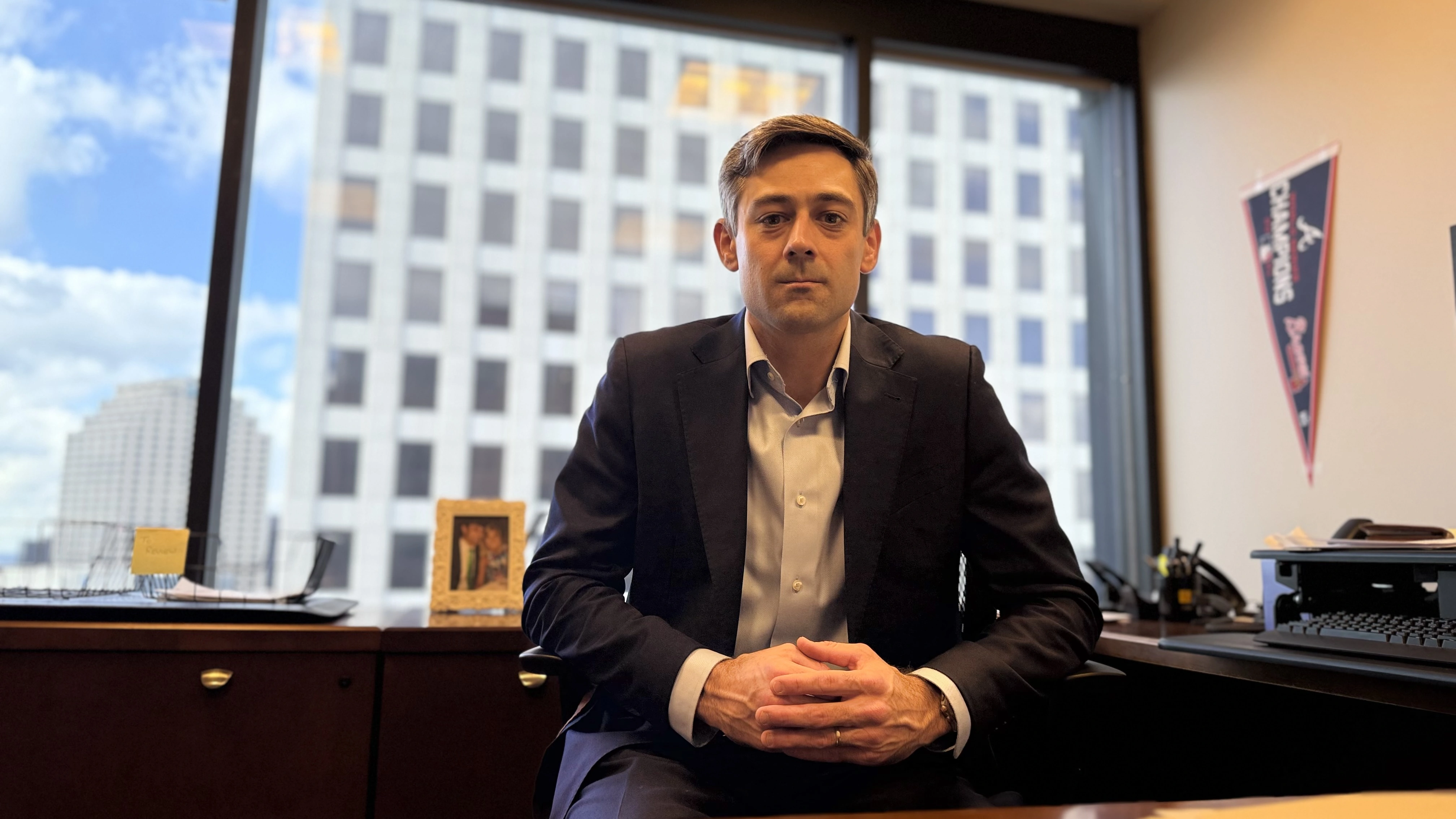 A professional-looking man in a suit sits at a desk in an office, appearing focused and ready to provide legal services.