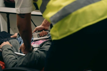 An emergency medical worker attends to an injured person on the ground, providing first aid and care.